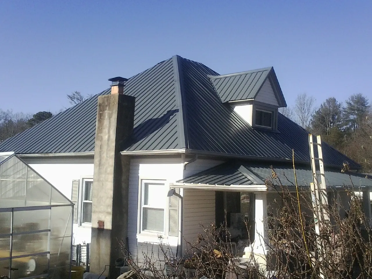 Dark blue standing seam metal roof on a white farmhouse with dormer in Rupert