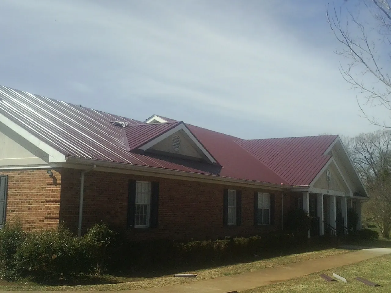 Red metal roof with gabled entries on a long brick building, from a Hail Damage Roof Repair job in Rupert