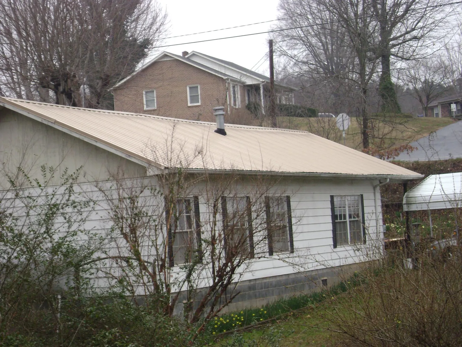 Tan metal roof on a white sided house set into a hillside — Commercial Roofing by Roofing Brothers in Rupert